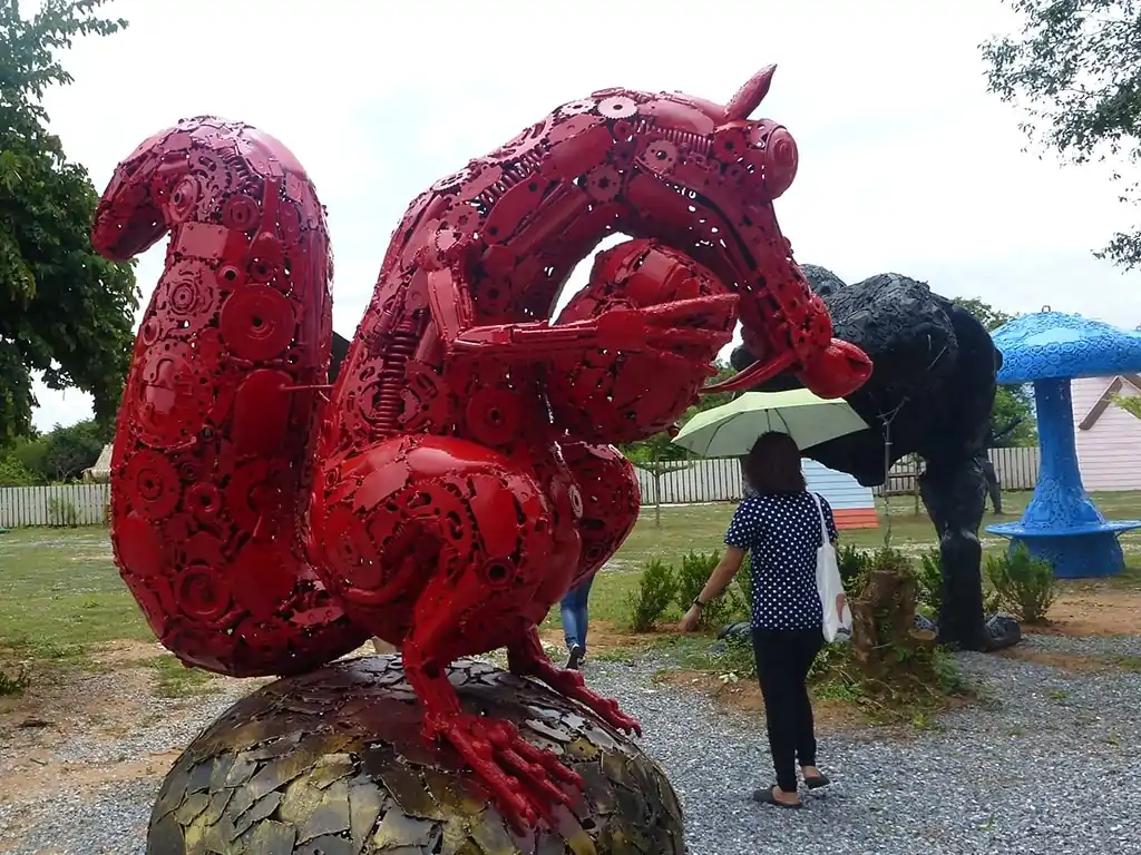 Opera d'arte: drago in metallo che sembra aggredire i passanti in un parco pubblico